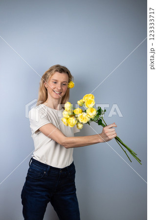 on light gray background a young blonde girl in a light T-shirt throws peony roses in front of her March 8 yellow flowers for separation smile on her face on light gray background a young blonde girl in a light T-shirt throws peony roses in front of her March 8 yellow flowers for separation smile on her face 123333717