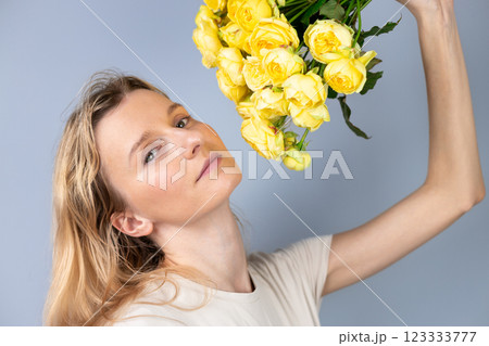 light gray background a young blonde girl with a large bouquet of yellow peony roses women's holiday March 8 first date the girl stands with her back turned to the side watch on camera 123333777