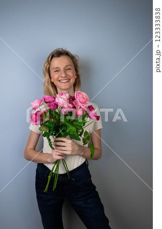 on a light gray background a young blonde girl with a large bouquet of pink peony roses women's holiday March 8 first date emotions on the face smiling girl on a light gray background a young blonde girl with a large bouquet of pink peony roses women's holiday March 8 first date emotions on the face smiling girl 123333838