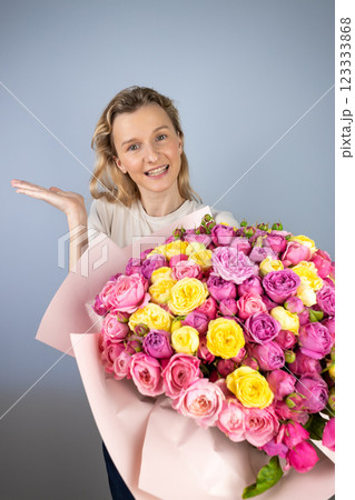 closeup gray background a young blonde girl with a large bouquet of pink peony roses women's holiday March 8 first date smiling raised palm to the side 123333868