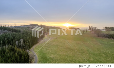A Serene Sunset Over Lush Green Fields and Forests, an ideal scene to unwind and relax in nature 123334834
