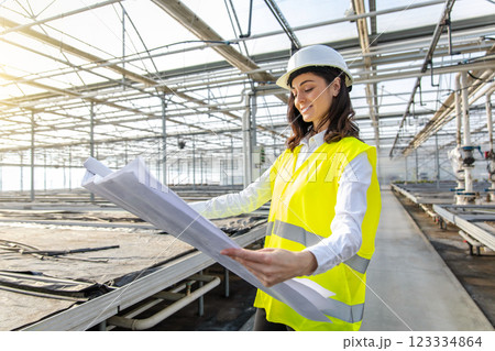 Female engineer in a greenhouse construction site scrutinizing a sketch Female engineer in a greenhouse construction site scrutinizing a sketch 123334864