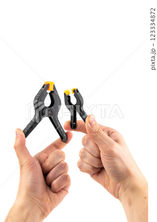 close up on white background, two male hands hold a large and a small plastic black clamp with an orange lock, a tool in everyday life, a reliable fixation, a repair tool close up on white background, two male hands hold a large and a small plastic black clamp with an orange lock, a tool in everyday life, a reliable fixation, a repair tool 123334872