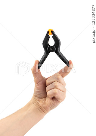 close-up on white background, a man's hand holds a large plastic black clamp with an orange lock, a tool in everyday life, a reliable fixation, a repair tool close-up on white background, a man's hand holds a large plastic black clamp with an orange lock, a tool in everyday life, a reliable fixation, a repair tool 123334877