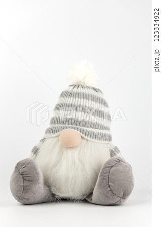 close-up on white background there is a toy under the Christmas tree gray round gnome with a large striped hat covering the eyes modern cartoon christmas decor close-up on white background there is a toy under the Christmas tree gray round gnome with a large striped hat covering the eyes modern cartoon christmas decor 123334922