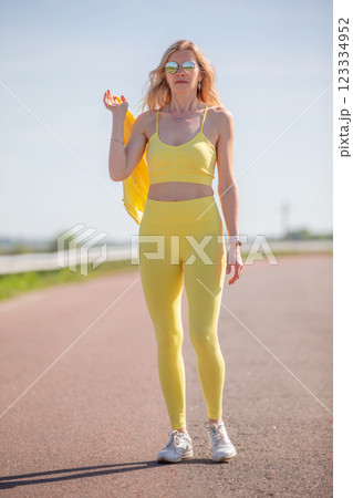 A middle-aged woman in a yellow sports outfit walks along the road. A middle-aged woman in a yellow sports outfit walks along the road. 123334952