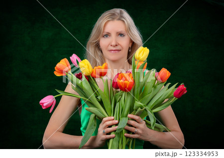 A beautiful adult woman with a bouquet of flowers on a dark background. 123334953