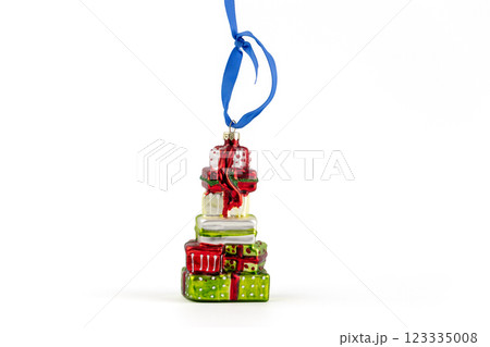 on white background stands a glass enameled Christmas tree toy in the shape of a stack of gifts in wrapping paper hanging blue ribbon modern decor toys with sparkles 123335008