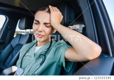 Female nurse sitting in a car and having a headache 123335195
