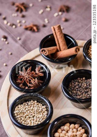 close-up on wooden board there is a set of black clay plates with different fragrant spices oriental seasonings for cooking a variety of round peppers cinnamon cardamom chickpeas 123335198