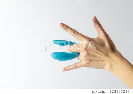 on white background on women's fingers blue vibrator for double penetration pleasure for two waterproof modern device variety for a couple partner replacement 123335252
