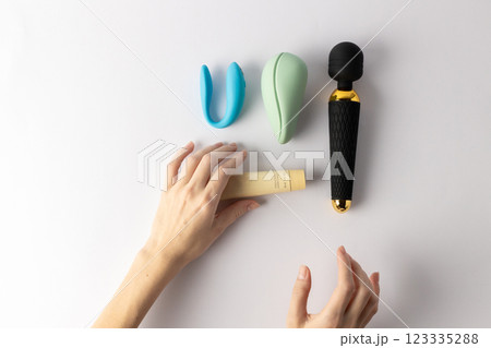 on white background, a woman s hand holds a large black vibrator in the shape of a microphone, lubricant in a tube, a vacuum mint and double blue vibrators lie nearby, various sex toys on white background, a woman s hand holds a large black vibrator in the shape of a microphone, lubricant in a tube, a vacuum mint and double blue vibrators lie nearby, various sex toys 123335288