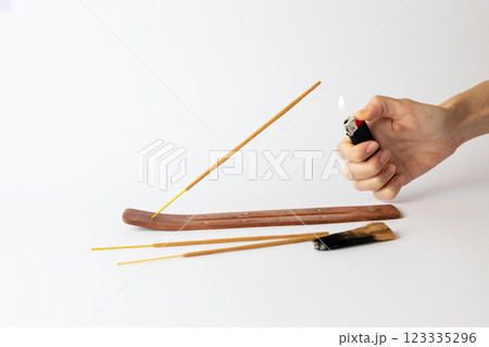 close-up on white background on a long brown stand with stars for incense sticks a new beige palosanto meditation stick is placed a hand with a black lighter setting fire close-up on white background on a long brown stand with stars for incense sticks a new beige palosanto meditation stick is placed a hand with a black lighter setting fire 123335296