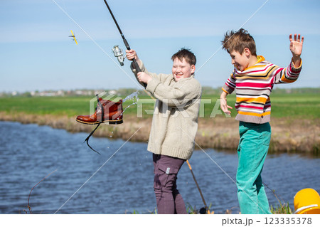 Funny fishing. Two of the boy's friends hooked an old shoe with a fishing rod and are laughing. 123335378