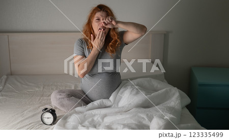 Caucasian pregnant woman sits on the bed and yawns. Insomnia. Caucasian pregnant woman sits on the bed and yawns. Insomnia. 123335499