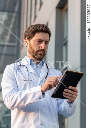 Ginger man in a lab coat with a tablet in hands looking determined 123335637