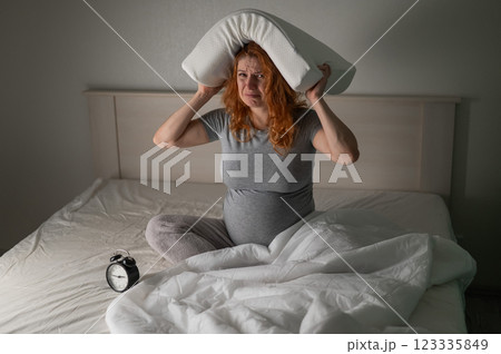 Caucasian pregnant woman sits in bed, holds a pillow on her head and cries. Insomnia. Caucasian pregnant woman sits in bed, holds a pillow on her head and cries. Insomnia. 123335849