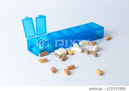 white background two bright blue pill boxes with a couple of open lids for taking pills, health care, partial filling, different shapes and colors of pills and vitamins pills lie next to the table 123335880