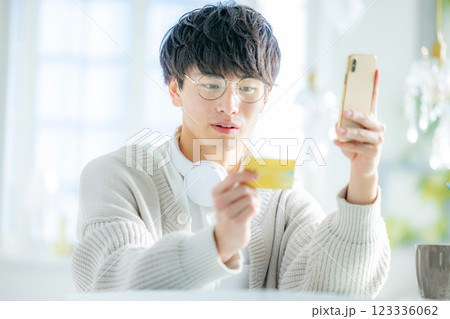 スマホとクレジットカードを見る若い男性 123336062