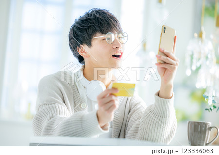 スマホとクレジットカードを見る若い男性 123336063