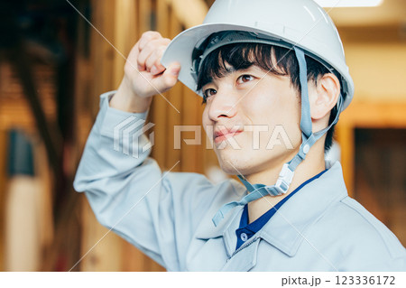 建設現場で働くヘルメットを被り作業着を着た若い男性 123336172