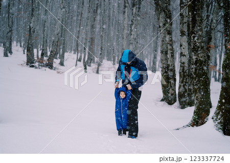 Dad stands with a small child holding hands under a snowfall in the forest 123337724