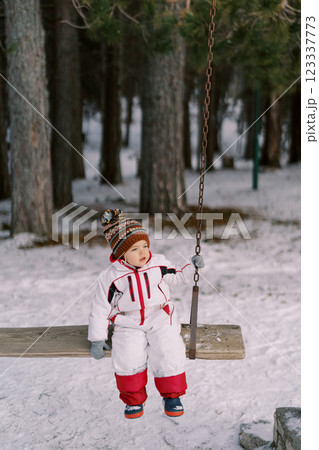 Little girl sits on a wooden swing in the forest and looks away 123337773