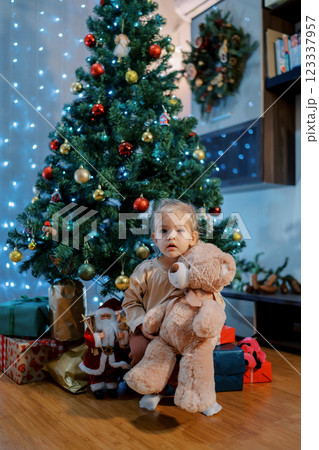 Little girl sits under a Christmas tree hugging a teddy bear 123337957