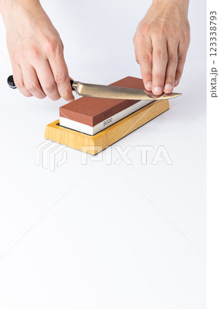 close up on white background on a table, man hands sharpen a steel knife protection against cuts, a red medium-hard stone for sharpening knives close up on white background on a table, man hands sharpen a steel knife protection against cuts, a red medium-hard stone for sharpening knives 123338793