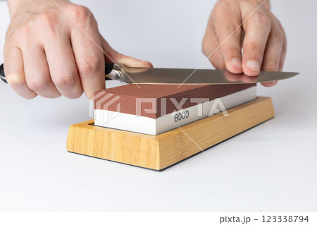 close up on white background on a table, man hands sharpen a steel knife protection against cuts, a red medium-hard stone for sharpening knives close up on white background on a table, man hands sharpen a steel knife protection against cuts, a red medium-hard stone for sharpening knives 123338794