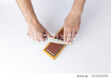 top shot on white background on a table, man hands sharpen a steel knife protection against cuts, a red medium-hard stone for sharpening knives 123338795