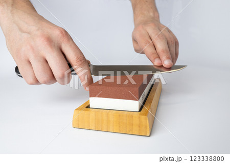 close up on white background on a table, man hands sharpen a steel knife protection against cuts, a red medium-hard stone for sharpening knives 123338800