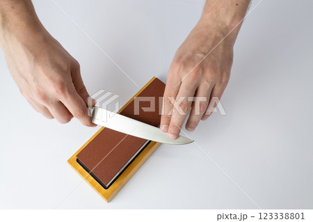 top shot on white background on a table, man hands sharpen a steel knife protection against cuts, a red medium-hard stone for sharpening knives 123338801
