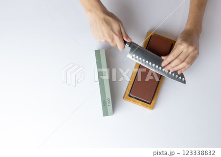 top shot on white background on a table, women's hands sharpen a steel knife, a lock under the arm, protection against cuts, a red medium-hard stone for sharpening knives green whetstone nearby top shot on white background on a table, women's hands sharpen a steel knife, a lock under the arm, protection against cuts, a red medium-hard stone for sharpening knives green whetstone nearby 123338832