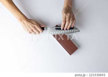 on white background on a table, women's hands sharpen a steel knife, a lock under the arm, protection against cuts, a red medium-hard stone for sharpening knives 123338843
