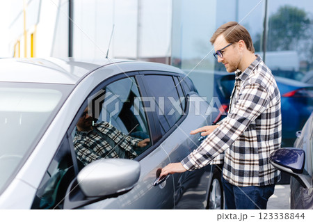 Young man buying auto at dealership salon and opening the door of his car 123338844