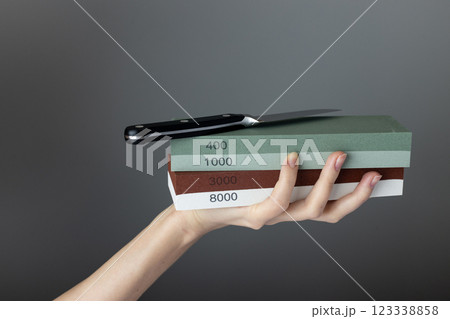 on a dark gray background in a woman's hand there are sharpening stones of different colors and abrasiveness, gradation of hardness, small steel knife on top of the stones 123338858