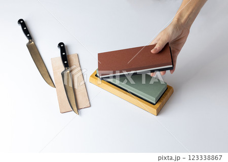 on white background on the counter lies the entire set of equipment for sharpening and polishing kitchen knives, the girl s hands hold a red stone of medium hardness, knives on the table on white background on the counter lies the entire set of equipment for sharpening and polishing kitchen knives, the girl s hands hold a red stone of medium hardness, knives on the table 123338867