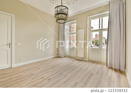 A spacious, elegantly designed room featuring large windows that allow ample natural light, complemented by neutral-toned walls and wooden flooring. 123339332