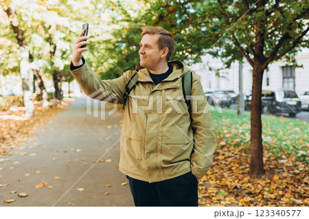 Smiling 30s man with backpack taking photo on park background. Selfie time. Holidays, rest, blogging banner. Charming male wearing stylish outfit have fine Smiling 30s man with backpack taking photo on park background. Selfie time. Holidays, rest, blogging banner. Charming male wearing stylish outfit have fine 123340577