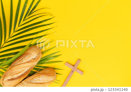 A wooden cross with a Bible and bread on a palm leaves pattern, a Palm Sunday theme A wooden cross with a Bible and bread on a palm leaves pattern, a Palm Sunday theme 123341140