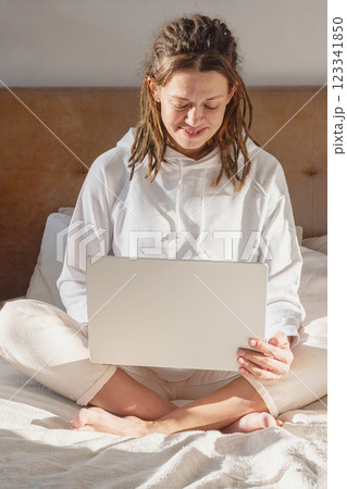 Woman Working Remotely Sitting on Bed with Laptop in the Morning. 123341850