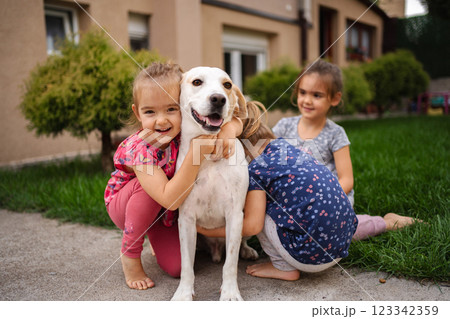 Children joyfully playing with a friendly dog in a sunny yard Children joyfully playing with a friendly dog in a sunny yard 123342359