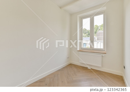 This interior room showcases a bright atmosphere with a large window allowing natural light, clean walls, and wooden flooring that accentuates minimalism. 123342365