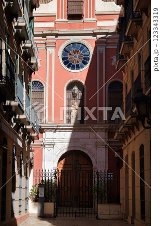 The image shows a view of a narrow alley leading to a brightly colored building, which appears to be a church or religious structure given the presence of a cross at the top and the architectural The image shows a view of a narrow alley leading to a brightly colored building, which appears to be a church or religious structure given the presence of a cross at the top and the architectural 123343319