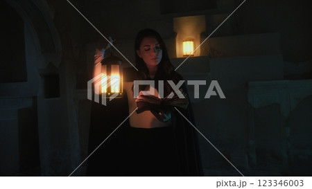 Woman Reads Mysteries On Magic Book In Ancient Cave At Night With Lantern Woman Reads Mysteries On Magic Book In Ancient Cave At Night With Lantern 123346003