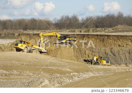 Yellow dump trucks and excavator are working in gravel pit 123346679
