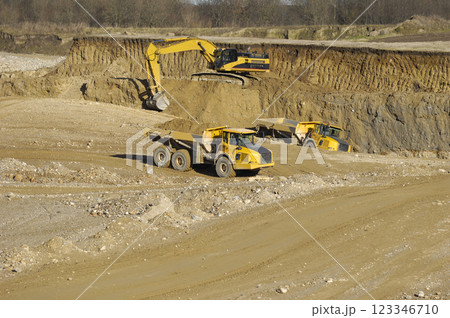Yellow dump trucks and excavator are working in gravel pit 123346710