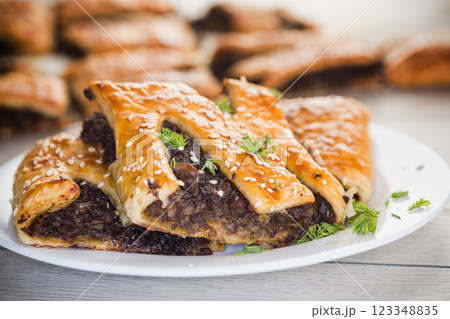 Golden puff pastries with mushroom filling and sesame seeds, on a light wooden table Golden puff pastries with mushroom filling and sesame seeds, on a light wooden table 123348835
