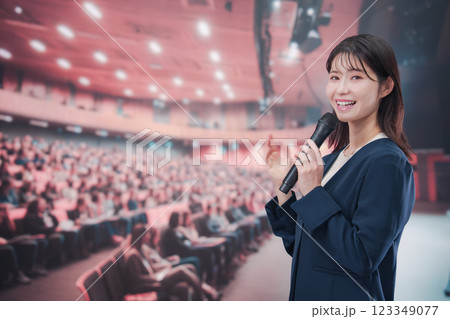大勢の聴衆が集まるホールで司会をする若い女性 大勢の聴衆が集まるホールで司会をする若い女性 123349077